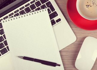 Blank notepad over laptop and coffee cup on office wooden table